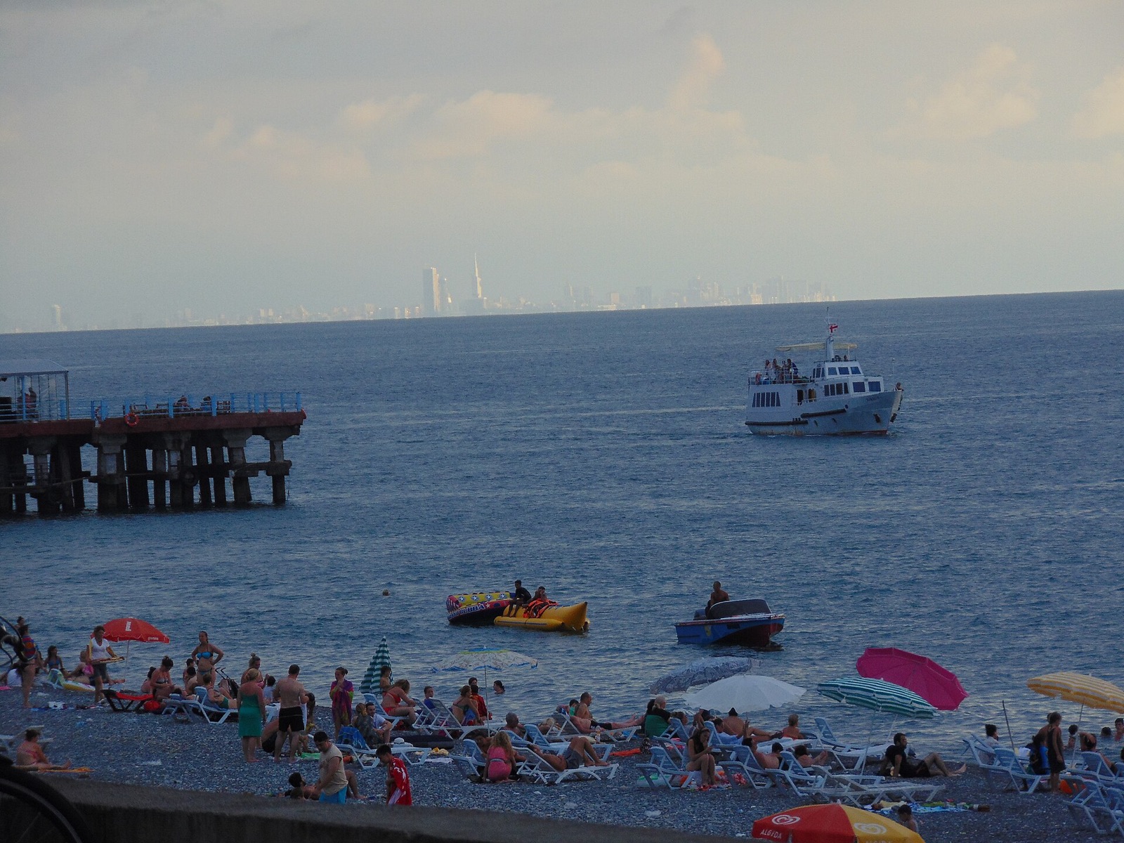 Bathers and small boats on the pebble beach at Kobuleti with the towers of the Batumi skyline on the horizon across the bay