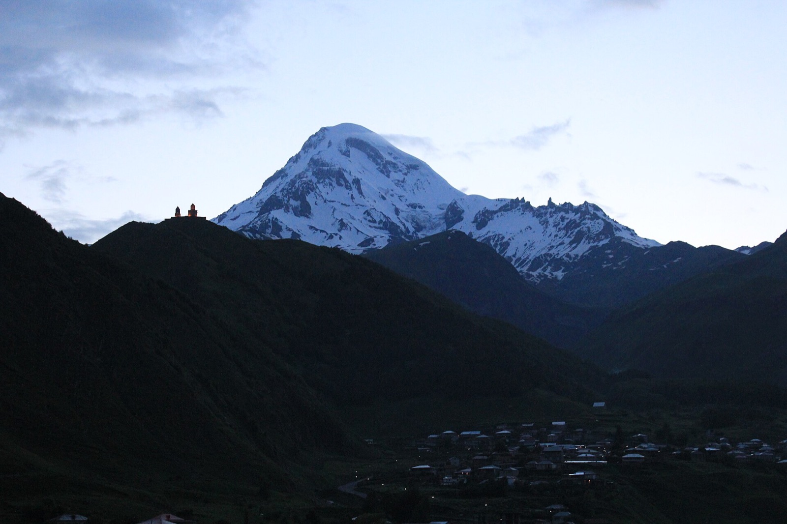 The Gergeti Trinity Church on its green spur above Stepantsminda with the snow-covered summit of Mount Kazbek behind